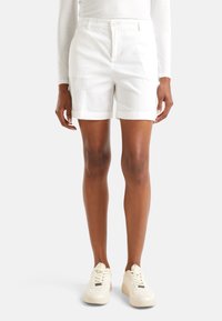 Bílé bavlněné kraťasy s přiléhavým střihem, ohrnutými manžetami a bočními kapsami, doplněné bílými botami na šněrování. Hladká textura.