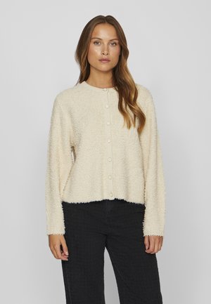 Weicher, cremefarbener Cardigan aus strukturiertem Material, mit langen Ärmeln und Rundhalsausschnitt. Verfügt über sechs Knopfverschlüsse auf der Vorderseite.