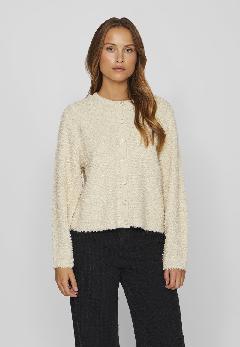Cardigan morbido color crema con un tessuto testurizzato, maniche lunghe e scollo rotondo. Presenta sei bottoni di chiusura sul davanti.