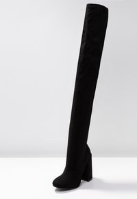 Bota negra por encima de la rodilla hecha de suave ante, con un tacón cuadrado alto, textura lisa y un diseño de punta redonda.