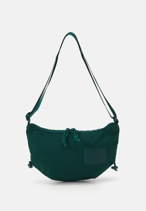 Sac à bandoulière en tissu vert à forme arrondie, fermeture par cordon de serrage et patch logo. Doté de bretelles réglables et d'une texture lisse.