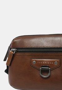 Borsa a tracolla in pelle marrone con chiusura a zip, hardware in metallo e dettaglio del logo. Texture liscia e forma rettangolare.
