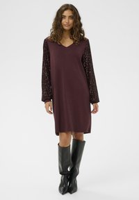 Abito bordeaux con scollatura a V e maniche lunghe decorate con paillettes, abbinato a stivali neri al ginocchio. Tessuto morbido, vestibilità comoda, lunghezza al ginocchio.