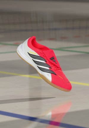 Zapatilla deportiva roja con parte superior de malla ligera, detalles en negro, talón blanco y suela de goma. Presenta un diseño aerodinámico y un ajuste ceñido.