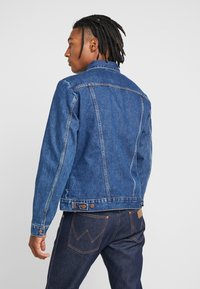 Niebieska dżinsowa kurtka o klasycznym wzorze, z kołnierzykiem, guzikami i wycięciem na plecach. Stylizowana z ciemnoniebieskimi dżinsami, podkreślającymi kontrastowe szwy.