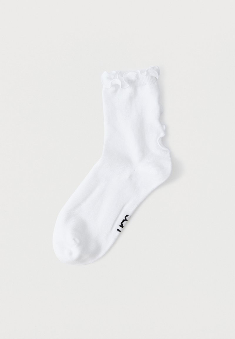 Λευκή κάλτσα αστραγάλου με βολάν στην κορυφή και μικρό μαύρο κείμενο κοντά στα δάχτυλα, απεικονισμένη σε απλό λευκό φόντο.