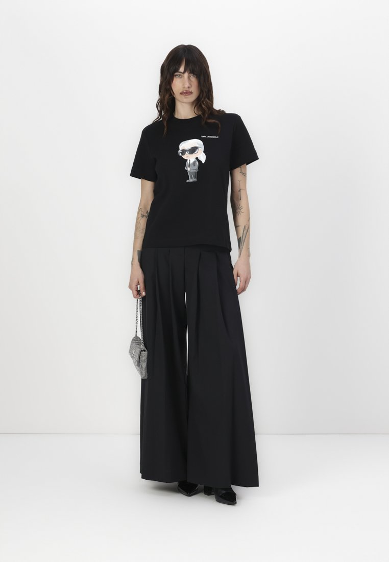 T-shirt noir en coton avec un design de cartoon à l'avant, associé à un pantalon large et taille haute noir et un petit sac à main en argent.
