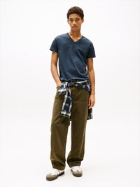 T-shirt v-neck marine, pantalon large vert olive, chemise à carreaux nouée à la taille, baskets blanches avec accents gris, textures de tissu lisses.