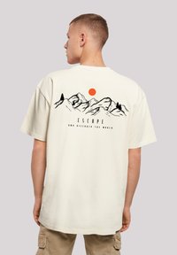 Cotton t-shirt in off-white, featuring a graphic of mountains, an orange sun, and the text "ESCAPE AND DISCOVER THE WORLD" on the back.