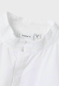 Blusa di cotone bianca con colletto rotondo, decorata con ricami a scallop e chiusura con bottone. L'etichetta della taglia indica 1½-2 anni.