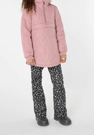 Roze doorgestikte pulloverjas met een hoge kraag, gecombineerd met zwarte broek met witte bloemenpatronen en zwarte laarzen.