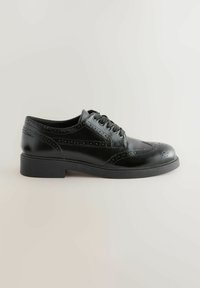 Musta nahkakenkä, jossa on brogue-yksityiskohtia, kuusi nauhakohtaa ja matala kumipohja. Ominaisuuksina sileä pinta ja klassinen muodollinen muotoilu.