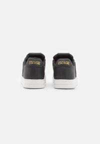 Black leather sneakers with white sole, featuring a padded collar and gold "VERSACE JEANS COUTURE" logo on the heel.