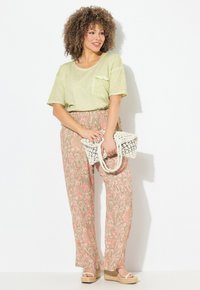 Top corto verde chiaro a maniche corte con dettaglio tasca, abbinato a pantaloni ampi a fantasia nei toni del rosa e del beige, e indossa una borsa intrecciata e sandali con platform.