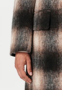 Wollmischungmantel mit einem karrierten Muster in Braun-, Creme- und Schwarztönen. Auffällige Details sind eine Fronttasche und eine weiche Textur.