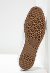 Semelle en caoutchouc marron avec motif de grip en diamant, semelle intermédiaire blanche et tige en toile jaune texturée. Logo "Converse ALL STAR" sur la semelle.