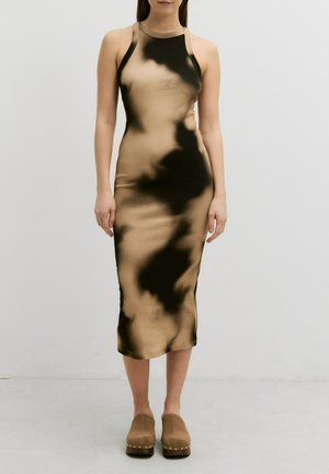 Figurbetontes, ärmelloses Kleid in einer Mischung aus beigen und schwarzen Batikmustern. Aus einem glatten Stoff gefertigt, knielang, kombiniert mit braunen Holzschuhen.