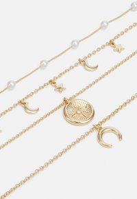 Gold-tone layered necklace set featuring pearl accents, star and crescent moon charms, with a central medallion engraved with a sunburst design.