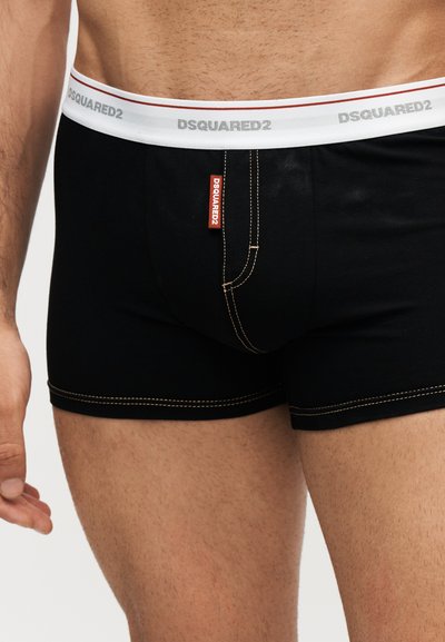 Buste masculin portant un boxer noir avec une ceinture blanche et le logo DSQUARED2 visible sur la ceinture et l’étiquette avant.