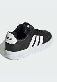 Crna cipela od sintetičke kože s bijelim prugama i logotipom, s čičak trakom, bijelim gumenim potplatom i teksturiranom gornjom površinom.