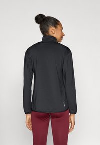 Fekete hosszú ujjú dzseki magas gallérral, sima textúrával és rugalmas szegéllyel, alul finom logóval díszítve.