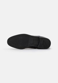 Suela de zapato negra con superficie de goma texturizada y marca grabada. Presenta una puntera redondeada y un diseño antideslizante para mejorar el agarre.