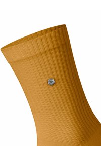 Calzino a coste giallo senape con un dettaglio a bottone argentato vicino alla parte superiore. La texture del tessuto appare morbida ed elastica.