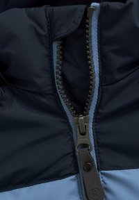 Blau und marinefarbene Steppjacke mit Reißverschlussdetails, ausgestattet mit Metallzähnen und einem dunklen Ziehband, aus glattem Stoff mit einer gesteppten Innentextur.
