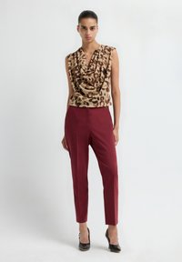 Top met kraag in luipaardprint in bruin en tan, gecombineerd met bourgondisch fitted broek. Model draagt zwarte high heels.