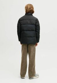 Svart pufferjakke med quiltemønster, høy krage og innsydde ermer. Kombinert med lysebrune, vide kordfløyelsbukser og joggesko.