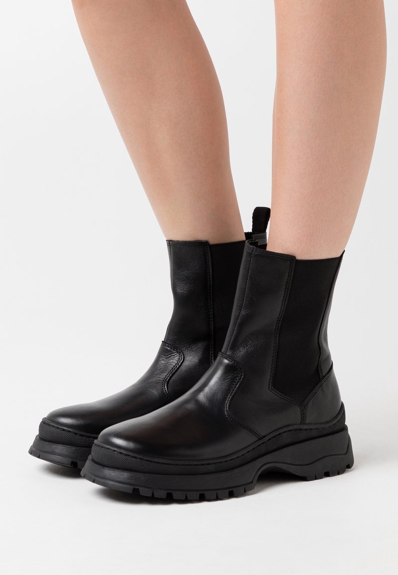 Svarta ankelstövlar i läder med elastiska sidopaneler, rund tå, tjock gummisula och dragflik bak för enkel påtagning.