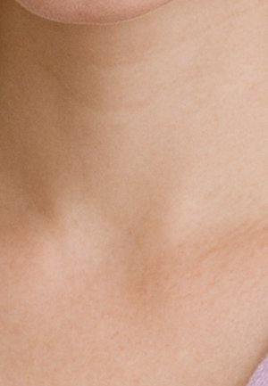 Gros plan sur le cou nu et la partie supérieure de la poitrine d'une personne, avec une peau lisse et un soupçon d'un vêtement violet sur le bord.