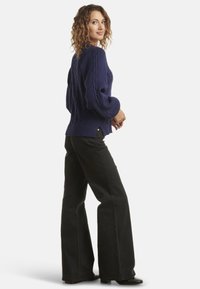 Navy cable-knit sweater with balloon sleeves, side slits, and ribbed hem paired with black flared pants and ankle boots.
