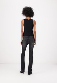 Top negro sin mangas combinado con jeans oscuros de campana con detalles desgastados. El atuendo presenta una textura suave y un diseño ajustado.