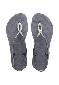 Infradito grigi con suole in gomma testurizzata e cinturini intrecciati in argento. Presentano un logo circolare sulla soletta vicino al perno delle dita.