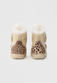 Tan ankelstøvler med leopardmønsterpanel, bløt hvit pelsfôr øverst, og en teksturert beige gummisåle.