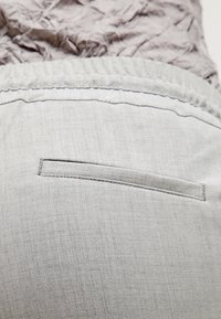 Ljusgrått tyg med en slät yta. Inkluderar en horisontell ficka med en smal sömöppning längs midjan.