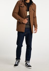 Abrigo de lana marrón con hombreras, cierre de cremallera y botones. Combinado con un suéter gris estampado y jeans de mezclilla oscuros. Zapatillas negras y blancas.