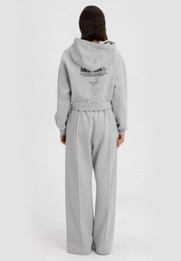 Grijze oversized hoodie en bijpassende wijdvallende sweatpants, met een trekkoordkap en riemdetail, voorzien van geprinte branding op de achterkant.