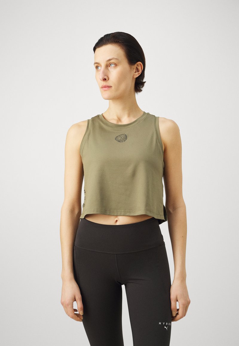 Õlipruuni lühikese lõikega tank top, millel on ümmargune kaelus ja logo detail. Omab lõdva sobivust ja külgsekke. Ühildub mustade kõrge vöökohtadega legginsitega.