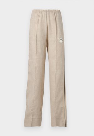 Slank stående kvinde med kort hår iført hvid cropped kortærmet top, beige vidde bukser med sidelange striber og beige sneakers.