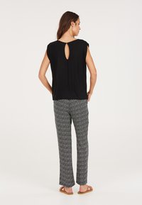 Top corto nero con dettagli a chiave sulla schiena, abbinato a pantaloni dritti a fantasia bianco e nero. Le ciabatte completano l'outfit.