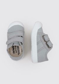 Baskets en toile grise avec deux brides Velcro, bout en caoutchouc blanc et semelles, arborant un design simple et une étiquette en coton biologique à l'intérieur.