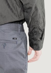 Chemise noire à motifs avec un design texturé et des boutons aux poignets, associée à un pantalon à motifs bleu marine avec une taille plate et des poches.
