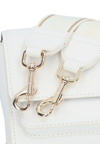 Λευκή δερμάτινη τσάντα με δύο χρυσές ελικοειδείς κλιπ και υφασμάτινη λωρίδα με υφή. Διαθέτει καθαρές γραμμές και λείο φινίρισμα.
