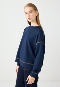 Granatowy sweatshirt o luźnym kroju z ściągaczami przy mankietach i u dołu. Posiada kontrastujące beżowe przeszycia wzdłuż szwów.