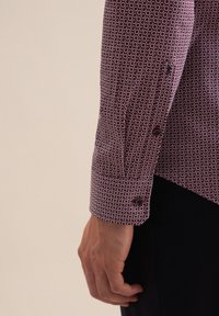Koszula z długimi rękawami w kolorze bordowym z wzorem w kółka, z kontrastowymi guzikami i teksturowanym materiałem. Widoczny detal mankietu.