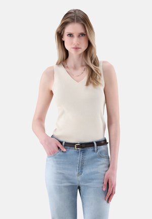 Top smanicato a costine crema con scollatura a V, indossato con jeans in denim azzurro chiaro e una cintura marrone scuro. Scollo e texture semplici.