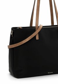 Sac fourre-tout noir en tissu texturé, avec des poignées en cuir marron et une fermeture éclair. Présente un logo doré en bas pour plus de détail.