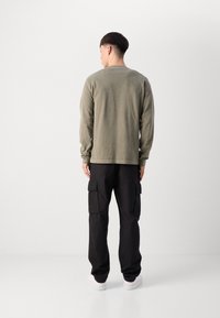 Camisa de manga longa verde-oliva, em tecido de algodão, ajuste descontraído, decote redondo. Calças cargo pretas, textura suave, bolsos laterais, combinadas com ténis brancos.